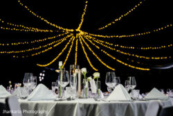 Elegant table setting with glassware and white napkins beneath string lights, ready for an event.