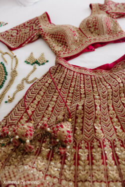 A red and gold embroidered traditional outfit with matching jewelry pieces displayed on a white surface.