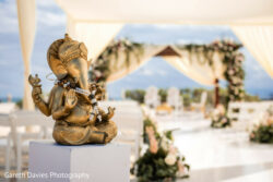 A bronze Ganesha statue sits on a pedestal at an outdoor wedding venue decorated with flowers and drapes.