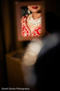 Close-up of a woman in red traditional attire and jewelry, her face reflected in a small mirror.