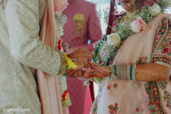 A bride and groom in traditional attire exchange rings during a wedding ceremony.